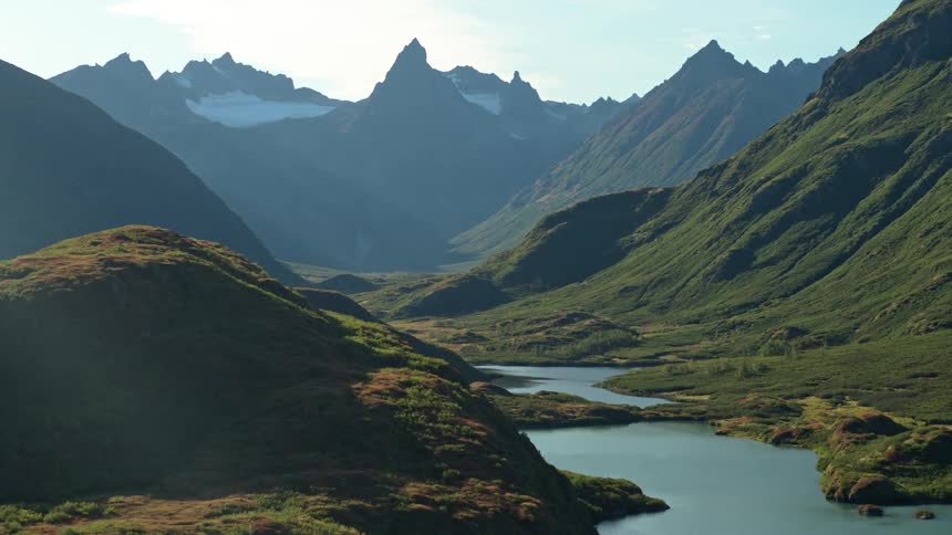 A slow zoom-out reveals a majestic mountain valley with a serene river winding through the lush, green landscape