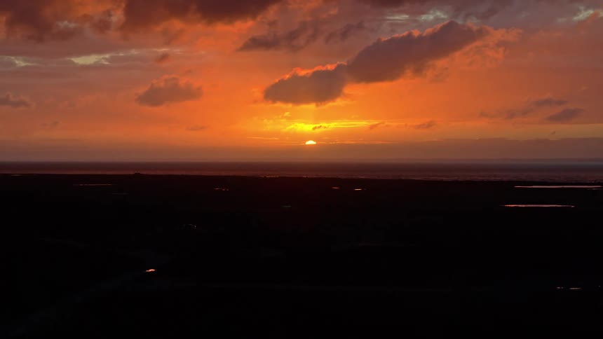 A stunning aerial view of a vibrant orange sunset over the ocean, with the coastal marshland silhouetted in the foreground