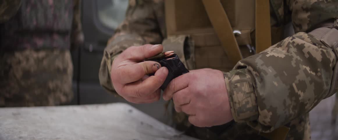 Slow motion close-up of a soldier in a camouflage uniform loading bullets into a rifle magazine