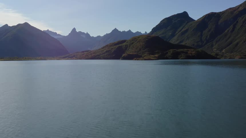 A calm lake peacefully ripples before a majestic mountain range under a clear sunny sky