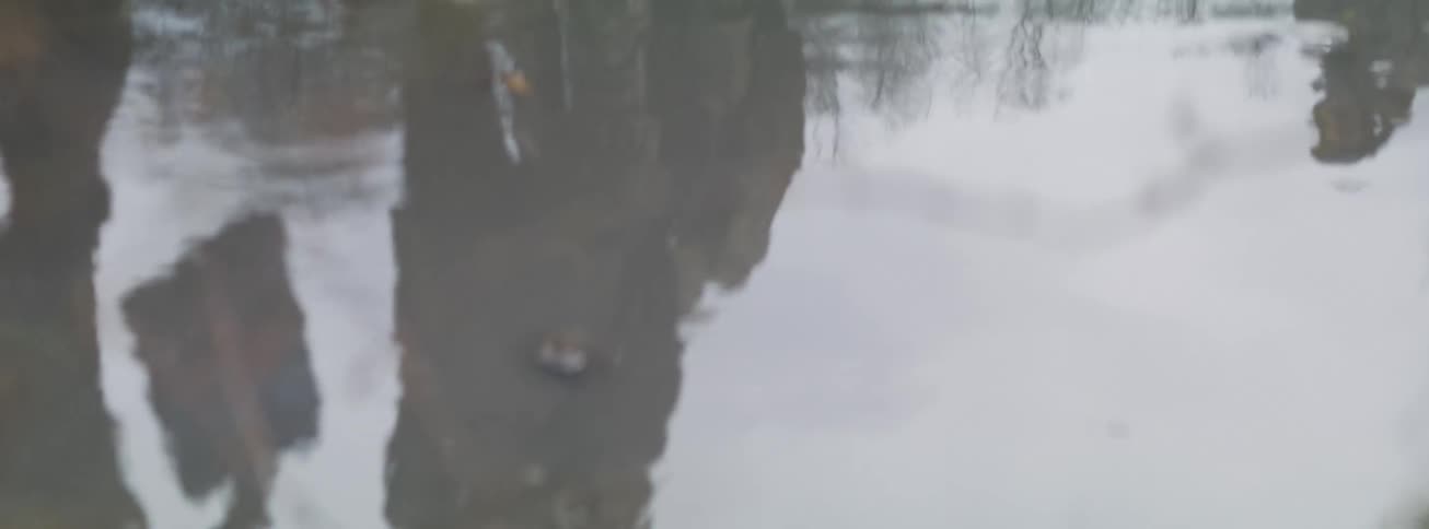 Artistic slow-motion shot of a person's reflection walking in the snow seen in a rippling puddle