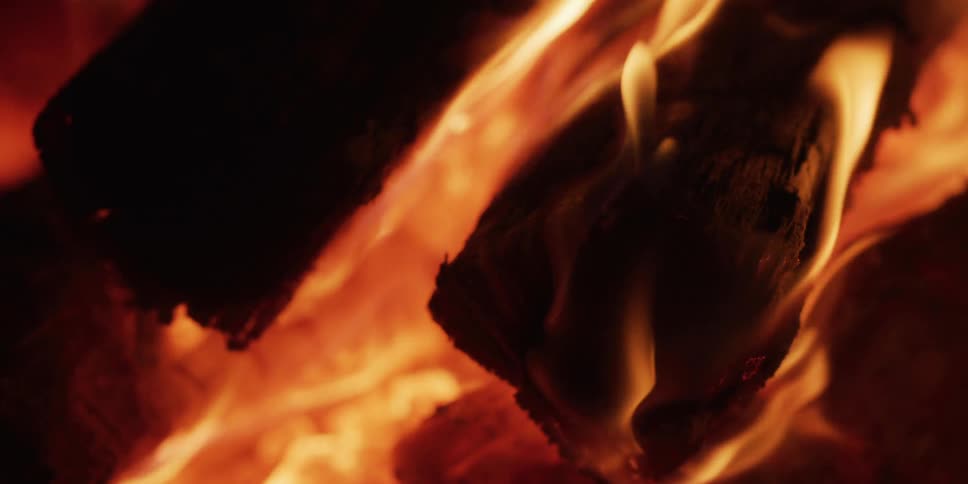 A mesmerizing close-up shot of fiery embers and slow-motion flames licking over burning logs