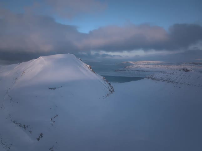 A majestic timelapse captures the changing light and moving clouds over a vast, snow-covered mountain landscape at dusk