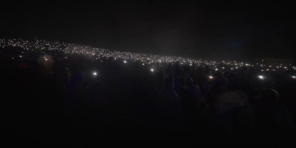 Spectators at a nighttime event light up the darkness with a sea of cell phone flashlights