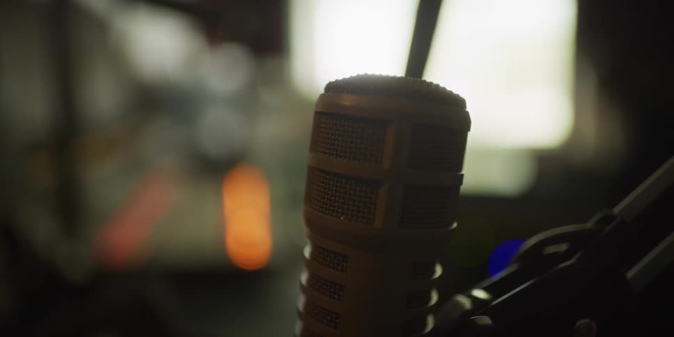 A close-up of a professional broadcast microphone sitting in a dimly lit studio with a soft, out-of-focus background
