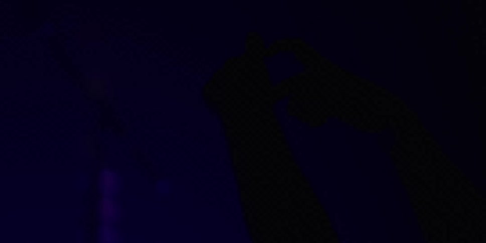 The silhouette of a person's hands making a heart shape against a hazy blue background at a concert