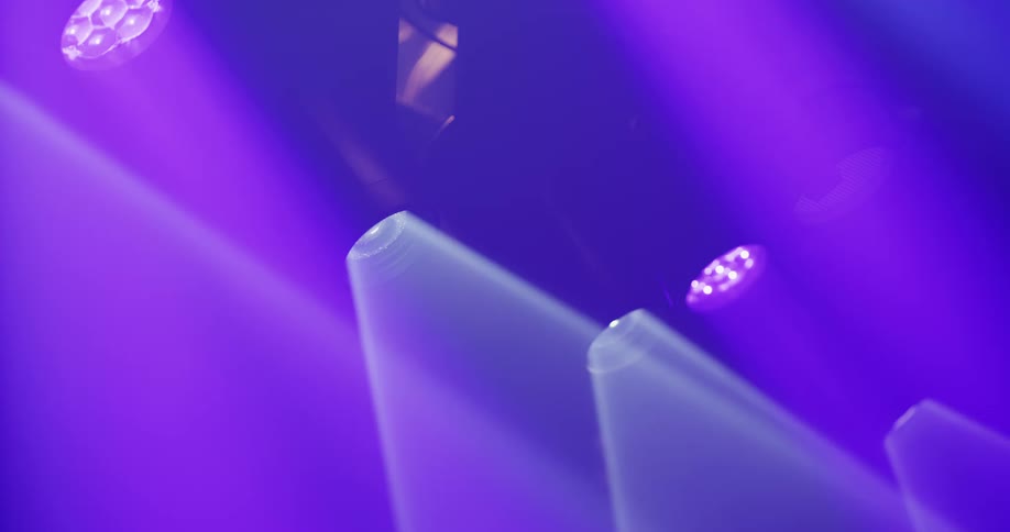 Close-up of purple stage spotlights casting bright beams through a hazy atmosphere