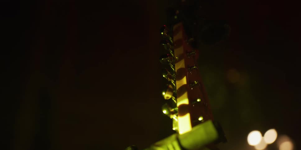 An atmospheric close-up shot of an electric guitar headstock on a stand illuminated by changing yellow and red stage lights in a dark venue