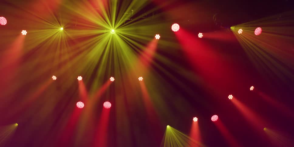 A dynamic array of red and yellow stage lights cast dramatic beams through a smoky atmosphere