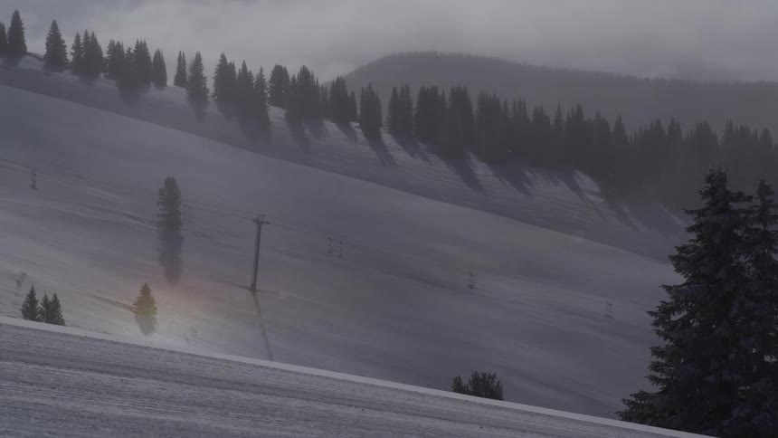 A serene sun dog glows on a misty, snowy mountain while snowflakes gently fall over an empty ski lift