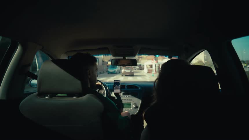 A couple navigates through town on a sunny day, as seen from the car's back seat