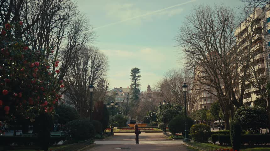 A woman stands alone on a beautiful tree-lined path in a European city park on a sunny day