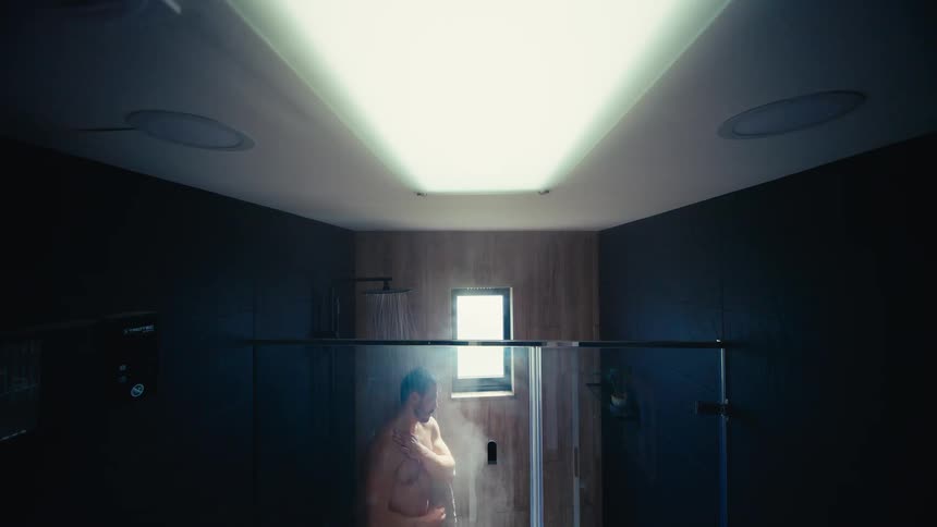 High-angle view of a man washing in a steamy shower in a dramatically lit, contemporary bathroom