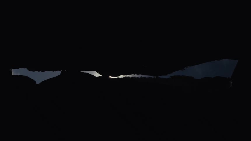 A bright sun shines with a starburst flare as it moves across a narrow opening in a dark silhouette