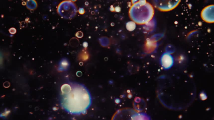 A dreamlike abstract animation shows vibrant, colorful bubbles and particles floating through a dark, cosmic background
