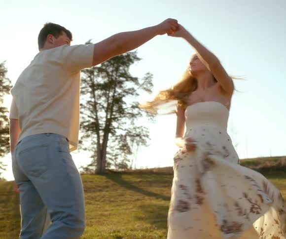 A happy young couple in love dances and spins together in a sunlit field in slow motion