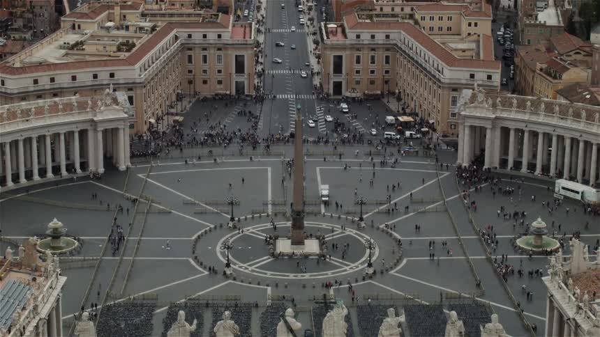 A large square in the middle of a city has many people walking around