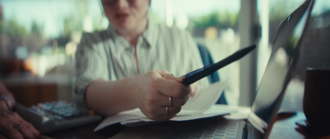 Close-up of a woman's hand pointing with a pen at a laptop screen while she works on her finances at home