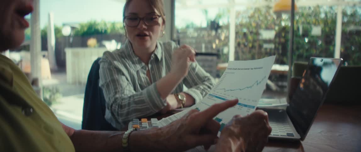 A financial advisor smiles as she explains a portfolio growth chart to her senior client in a sunlit modern home