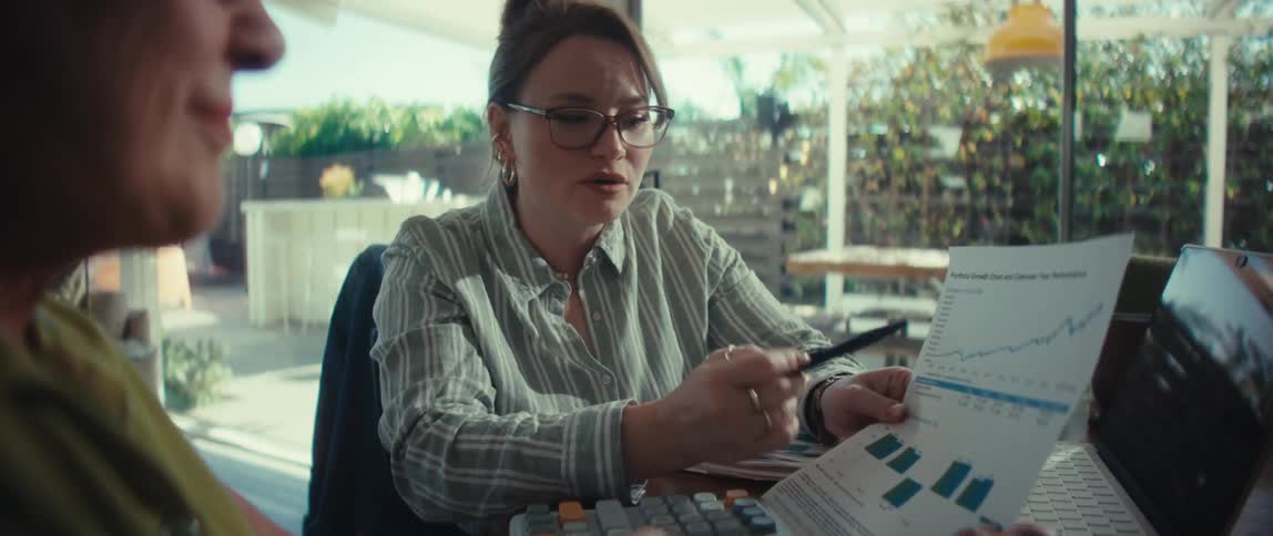 A financial advisor confidently explains a positive portfolio growth chart to her client during a meeting in a sunlit office