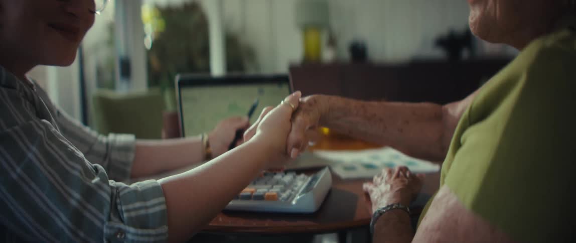 A young professional woman and an elderly woman smile and shake hands in agreement during a financial consultation at home