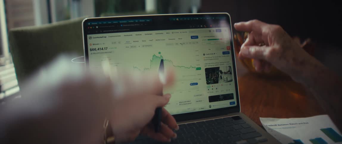 Two people discuss cryptocurrency market trends while analyzing a financial chart on a laptop
