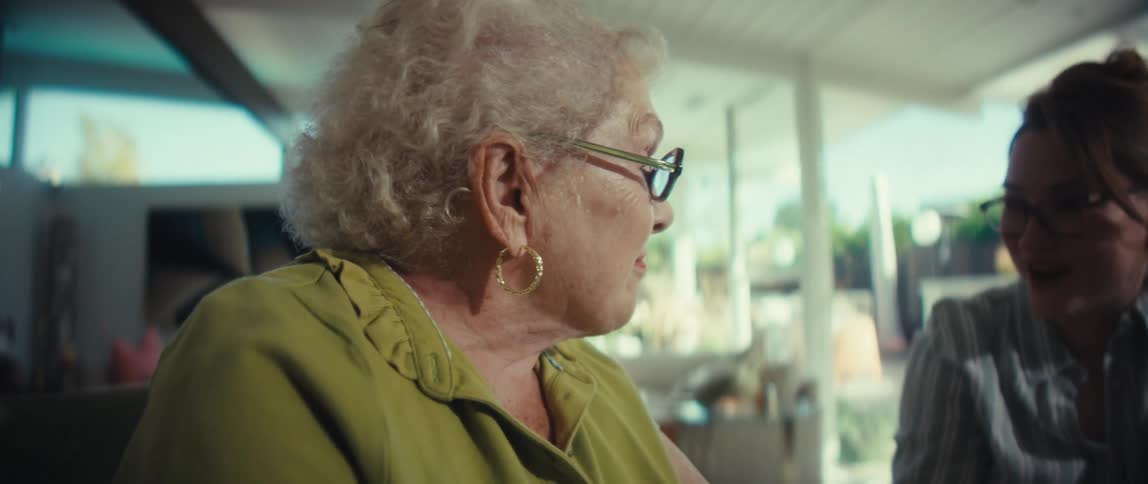 A young woman patiently explains a financial performance chart to a smiling elderly woman in a bright, modern home