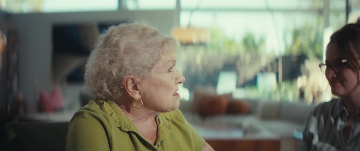 An elderly woman speaks passionately during a conversation with a younger woman in a modern home