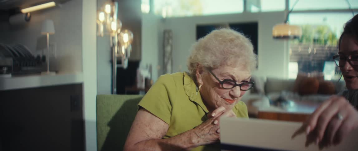 A young woman and an elderly woman shake hands in agreement, then the senior woman laughs with delight as she looks at something off-screen