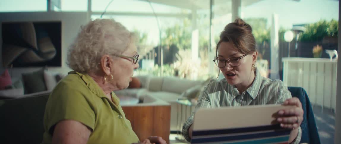 A compassionate advisor shakes hands and then holds an elderly woman's hand for support while reviewing documents together in a sunlit modern home