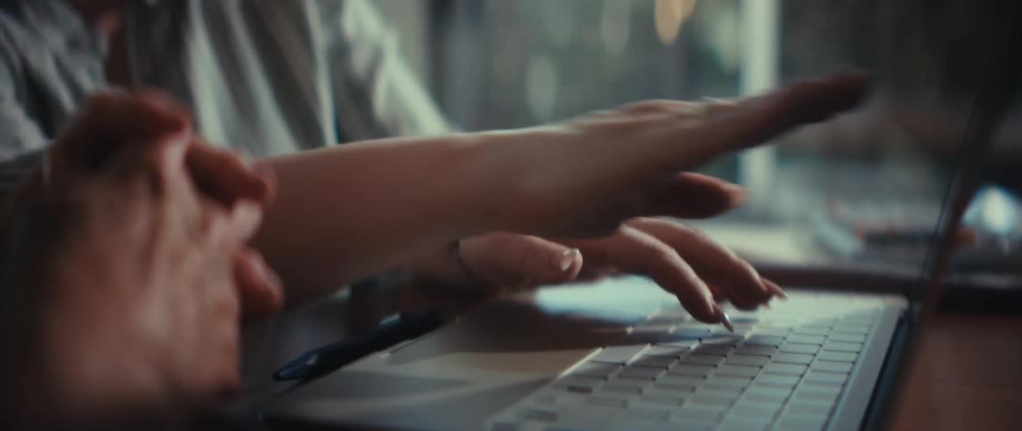 A young woman with glasses patiently teaches an older woman how to use a laptop in a close-up slow-motion shot