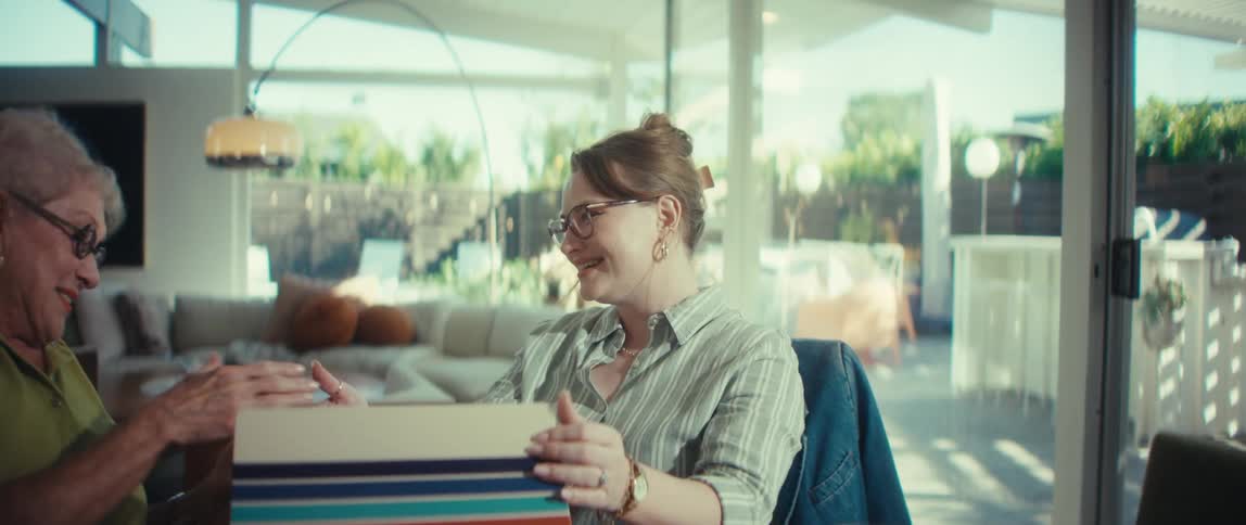 A young professional woman smiles and shakes hands with a senior client after a successful meeting in a modern, sunlit home