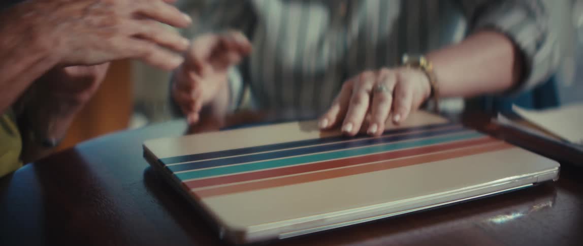 A close-up shot of a young woman comforting an older woman by holding her hand before opening a colorful striped laptop