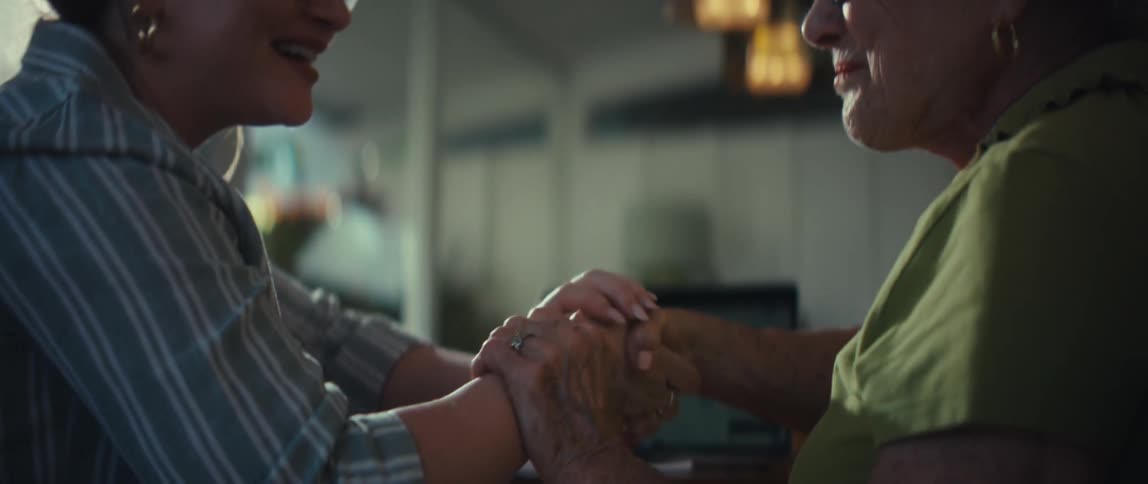 A daughter gently holds her elderly mother's hands for comfort during an emotional conversation at home