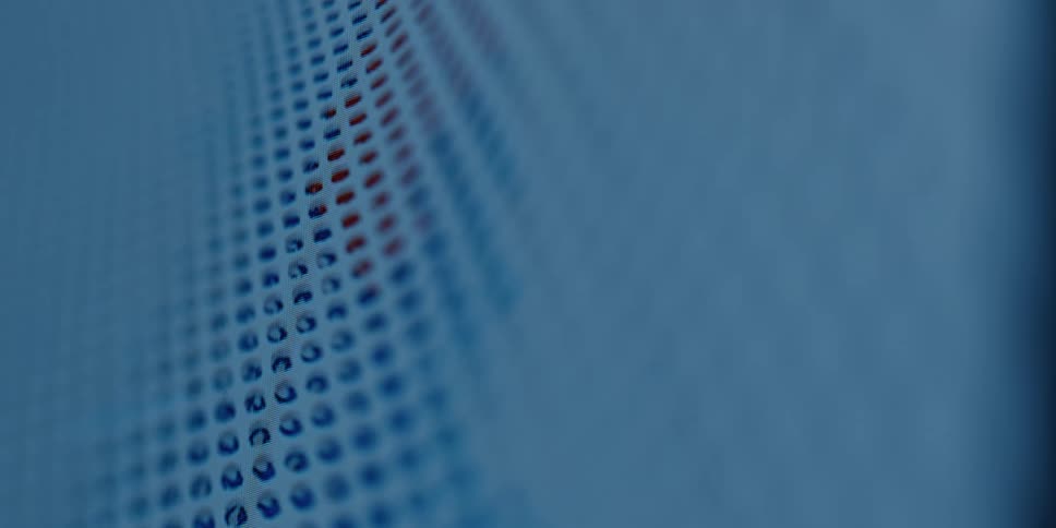 An abstract close-up shot of a blue perforated surface with red light briefly flashing behind it