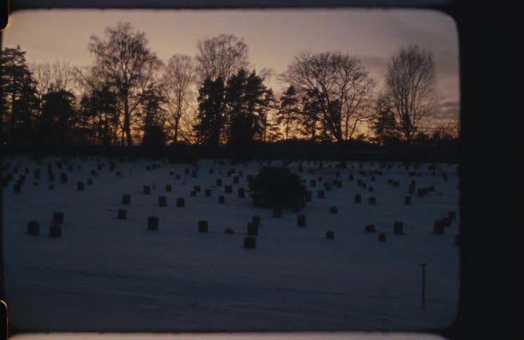 A somber, vintage film view of a snow-covered cemetery with rows of tombstones silhouetted against a beautiful winter sunset