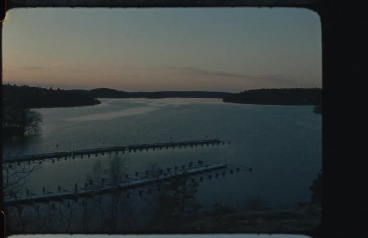 A serene, vintage film shot captures empty snow-dusted boat docks on a tranquil lake at twilight