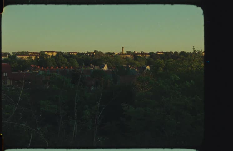 Vintage 8mm film captures a static wide shot of a European town nestled amongst lush trees during the golden hour