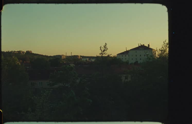 Authentic Super 8mm film captures a nostalgic view of a quiet European town at sunset, with treetops in the foreground