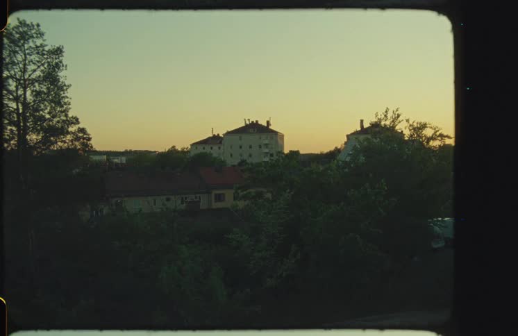 A vintage film view of a quiet residential neighborhood with houses and trees bathed in the warm glow of sunset