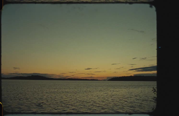 A vintage, super 8mm film shot of a tranquil lake with gentle waves during a serene sunset