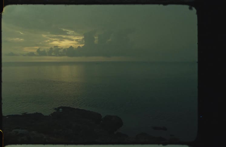 Vintage Super 8mm footage captures a moody, wide shot of the ocean horizon under a dark, cloudy sky at dusk