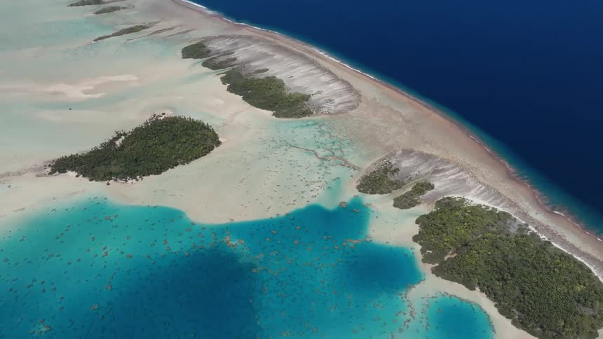 An incredible high-angle aerial view of a remote tropical atoll with turquoise lagoon waters and lush green islets