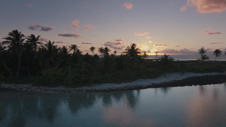 A stunning aerial view of a secluded tropical island with palm trees silhouetted against a golden sunset over the calm ocean