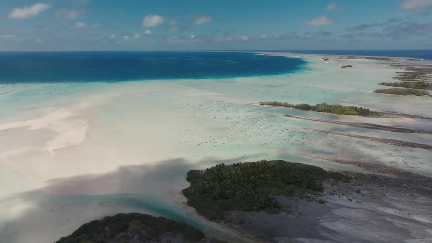 A stunning aerial view captures the vast expanse of a tropical atoll, where turquoise lagoons and white sandbars meet the deep blue ocean