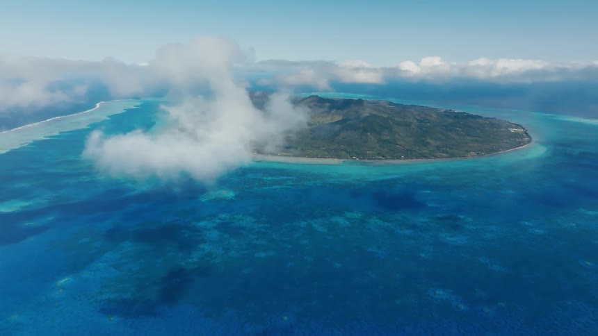 Stunning aerial view of a lush tropical island surrounded by a vibrant blue ocean and coral reefs, with clouds hovering above