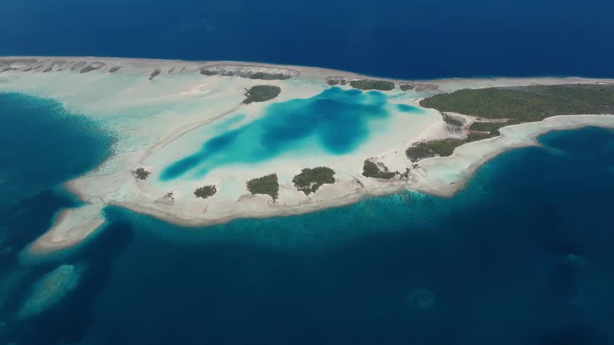 An awe-inspiring aerial shot showcases the breathtaking beauty of a tropical atoll surrounded by deep blue and turquoise waters