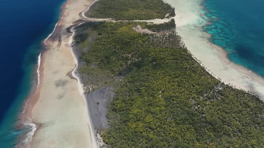 Static high-angle aerial view of a lush, tropical atoll separating the deep blue ocean from a shallow turquoise lagoon