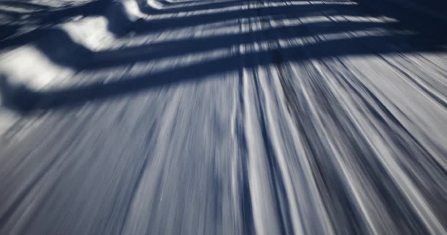 A fast-paced point-of-view shot traveling over a snowy road with motion blur and passing shadows