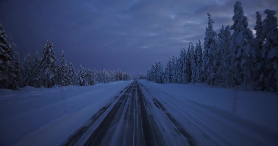 A point of view shot from a car driving through a snowy landscape during the polar night in Lapland